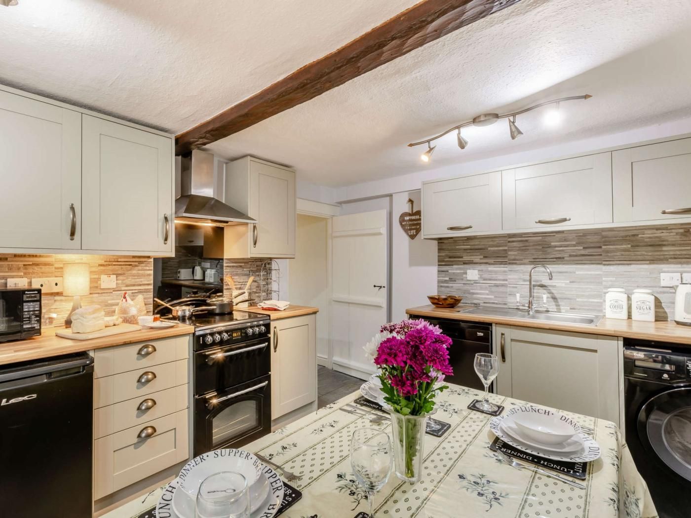 A modern kitchen with white cabinetry, a built-in oven, a microwave, and a dining area with a table set for a meal.
