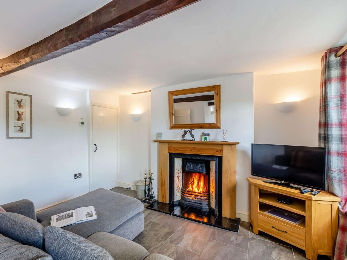 A living room with a fireplace, a sofa, a television, and a wooden ceiling beam.