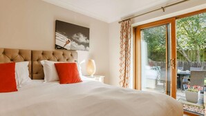A bedroom with a large bed, a headboard, a bedside table with a lamp, and a view through a glass door. - 3 Bed in Bideford (oc-89866) (Westward Ho!)
