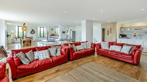 A spacious living area with red leather sofas, a dining table, and a kitchen in the background. - 5 Bed in Woolacombe (oc-89937) (Woolacombe)