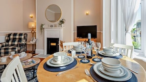 A dining area with a round table set for four, a fireplace, a television, and a plaid armchair. - 2 Bed in Swanage (oc-90116) (Swanage)