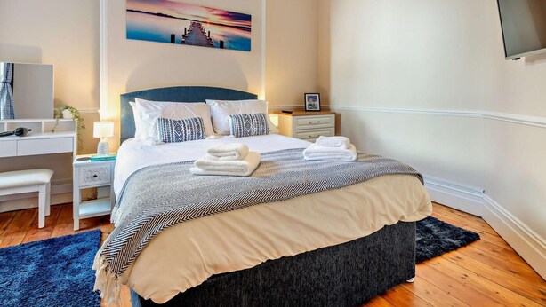 A hotel room with a bed, bedside tables, a desk, a chair, a TV, and a painting on the wall. - 2 Bed in Swanage (oc-90116) (Swanage)