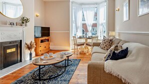 A living room with a fireplace, a television, a dining area with a table and chairs, and a sofa. - 2 Bed in Swanage (oc-90116) (Swanage)