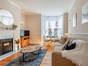 A living room with a fireplace, a television, a dining area with a table and chairs, and a sofa. - 2 Bed in Swanage (oc-90116) (Swanage)