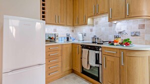 A kitchen with wooden cabinets, a white refrigerator, a stove, and a countertop with kitchen utensils. - 2 Bed in Swanage (oc-90116) (Swanage)