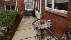 A patio with a mosaic table, a chair, and a potted plant. - 2 Bed in Swanage (oc-90116) (Swanage)