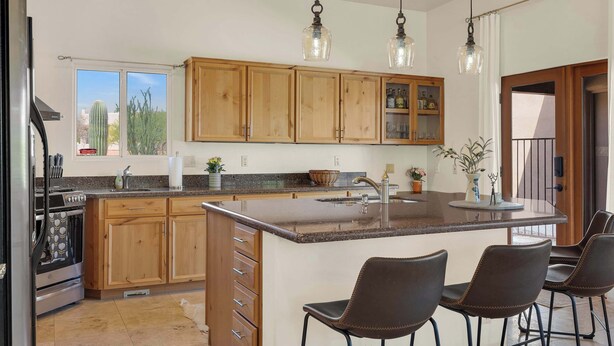 A kitchen with wooden cabinets, a granite countertop, a central island with bar stools, and pendant lighting. - The Desert Preserve Pool | Desert Views | Quiet Retreat (Tucson)