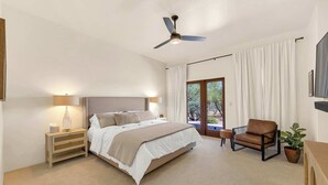 A bedroom with a bed, bedside tables, a chair, a ceiling fan, and a view through a large window. - The Desert Preserve Pool | Desert Views | Quiet Retreat (Tucson)