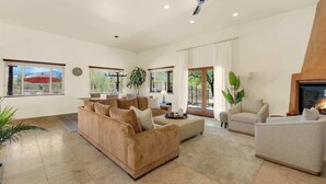 A spacious living room with a large sofa, a smaller armchair, a coffee table, and a fireplace. - The Desert Preserve Pool | Desert Views | Quiet Retreat (Tucson)