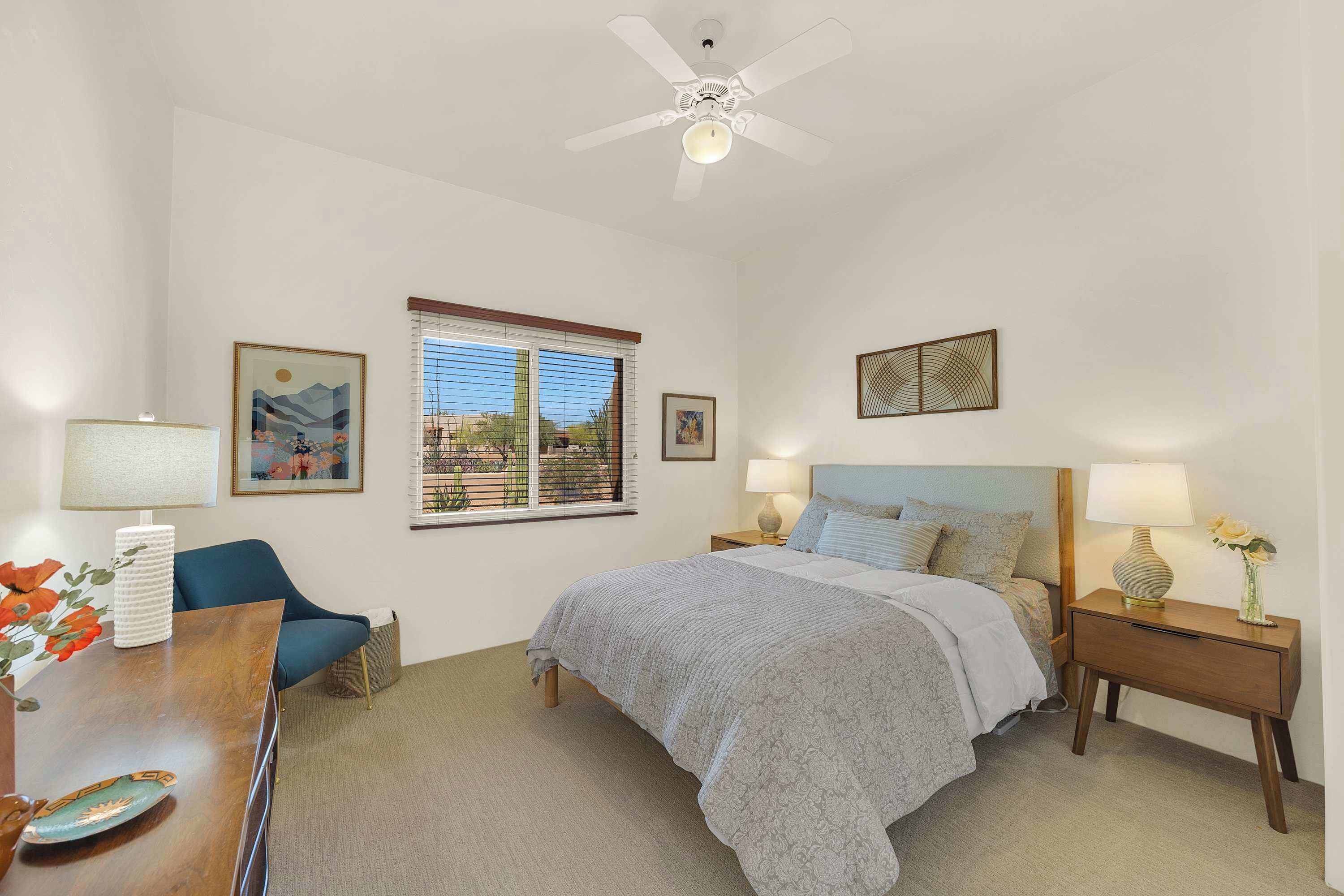A bedroom with a bed, two bedside tables, a chair, a desk, a window, and a ceiling fan.