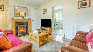 A living room with a fireplace, leather sofas, a TV, and a dining area visible through an open door. - 2 Bed in Hexham (oc-89299) (Kielder)