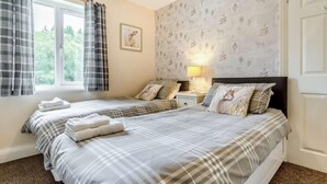 A bedroom with two beds, a window with curtains, a wall with a nature-themed wallpaper, and a bedside lamp. - 2 Bed in Hexham (oc-89299) (Kielder)