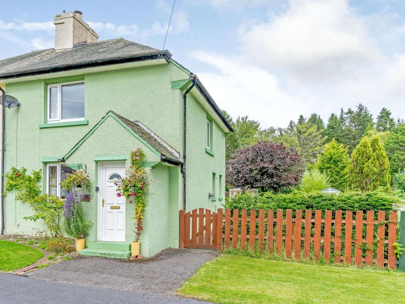 Une maison verte avec une porte blanche, un petit porche et une clôture en bois.