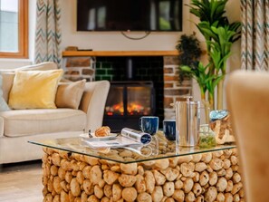 A living room with a glass coffee table, a sofa, a fireplace, and a television. - 3 Bed in Bideford (oc-89865) (Westward Ho!)
