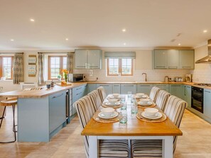A spacious kitchen with a central island, a dining area with a wooden table set for four, and light blue cabinetry. - 3 Bed in Bideford (oc-89865) (Westward Ho!)