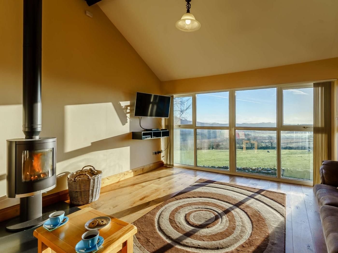 A cozy living room with a fireplace, a television, and a large window offering a view of the countryside.