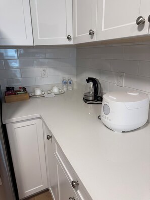 Una cocina con alacenas blancas, una cafetera y una tetera sobre la encimera.