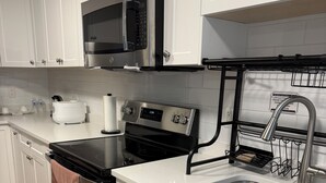 Moderni keittiö, jossa on valkoiset kaapit, ruostumattomasta teräksestä valmistetut kodinkoneet, mikroaaltouuni, uuni ja tiskiallas, jossa on astiateline.