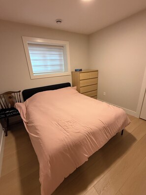 Un dormitorio con cama, cómoda, ventana con persianas y luz de techo.