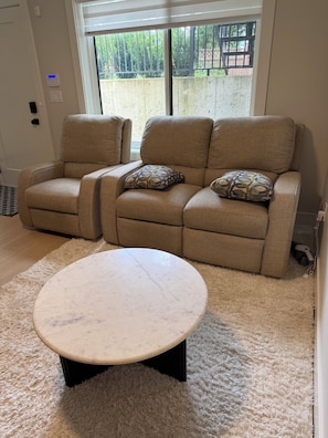 Una sala de estar con un sofá color beige, una mesa de centro redonda y vistas a través de una ventana.