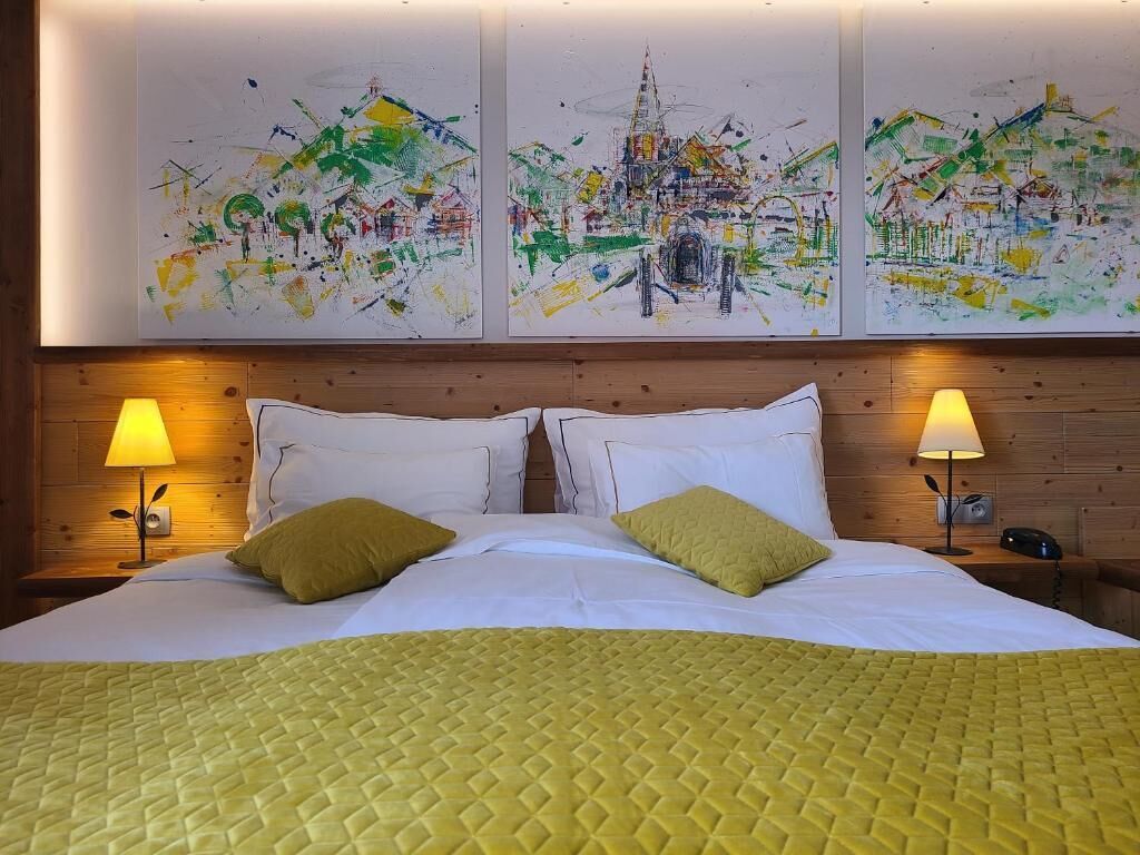 Quarto de hotel com uma cama grande, duas luminárias de cabeceira e três quadros abstratos na parede.