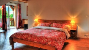 Una camera da letto con un letto di legno, due lampade sui comodini, una coperta con motivo rosso e vista attraverso una porta in vetro.
