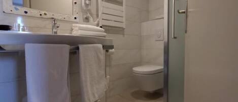 A bathroom with a sink, mirror, towel rack, toilet, and a shower area.