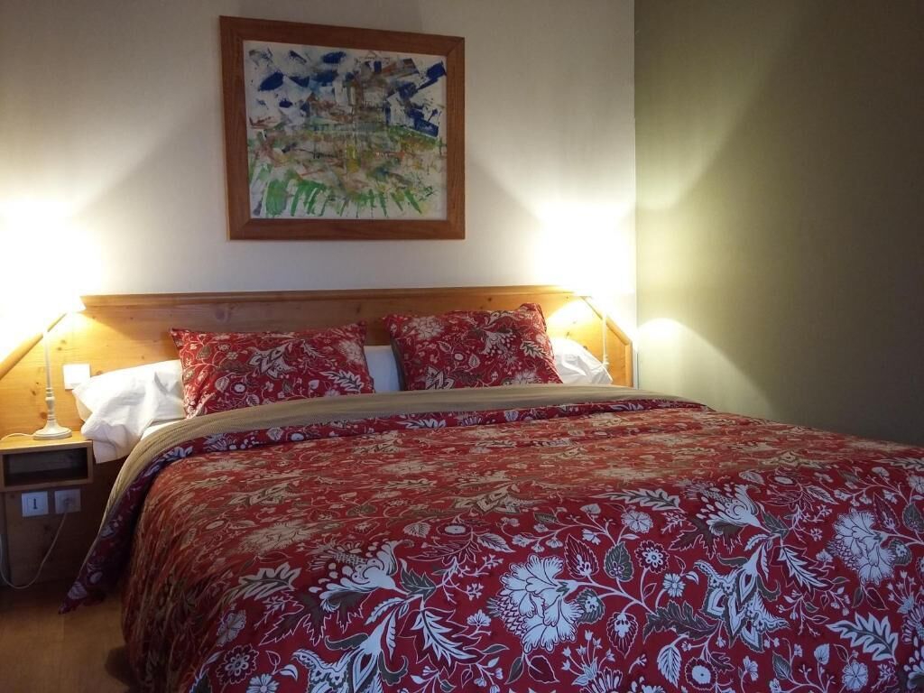 Una cama con colcha floral, una mesita de noche con lámpara y un cuadro en la pared.
