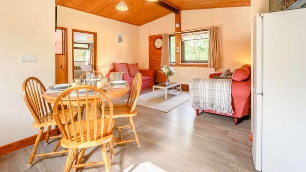 Une pièce chaleureuse avec un plafond en bois, une table à manger avec des chaises, un canapé, une petite table basse et un réfrigérateur.
