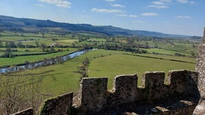 Un mur de pierre ancien, avec une rivière et des champs en arrière-plan.