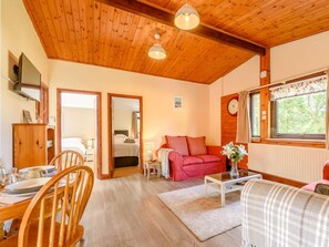 Ein gemütliches Zimmer mit Holzbalkendecke, einem Essbereich mit Tisch und Stühlen, einem roten Sofa und einem Fenster mit Blick ins Grüne.