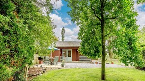 Un petit bâtiment en bois, avec une allée de gravier, entouré d’une végétation luxuriante et d’une clôture blanche en bois.