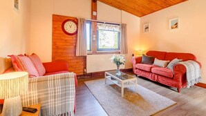 Un salon chaleureux avec un plafond en bois, un canapé rouge, un fauteuil rouge, une table basse en verre et une horloge au mur.