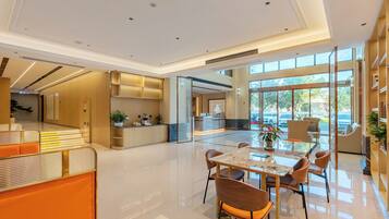 A modern hotel lobby with a reception desk, seating area, and a large window offering a view of the outdoors.
