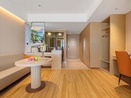Una habitación de hotel moderna con un sofá, una mesa redonda con un florero, un espejo y un armario de madera.