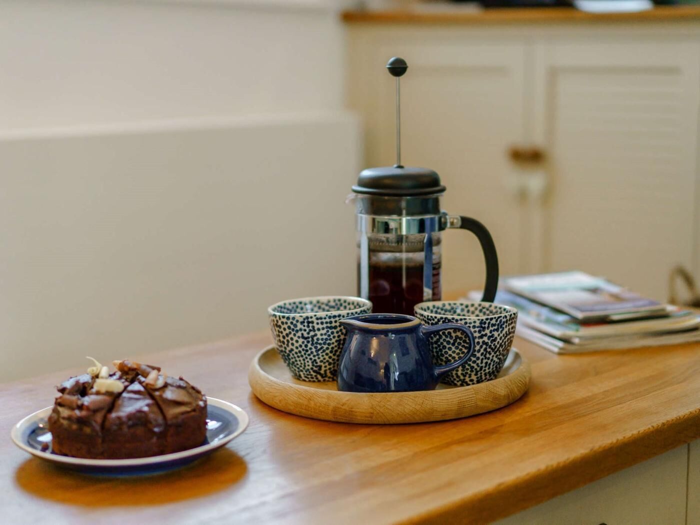 A coffee maker, cups, and a dessert on a wooden table.