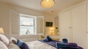Un dormitorio con cama, ventana con contraventanas, mesita de noche con lámpara, cómoda y armario.