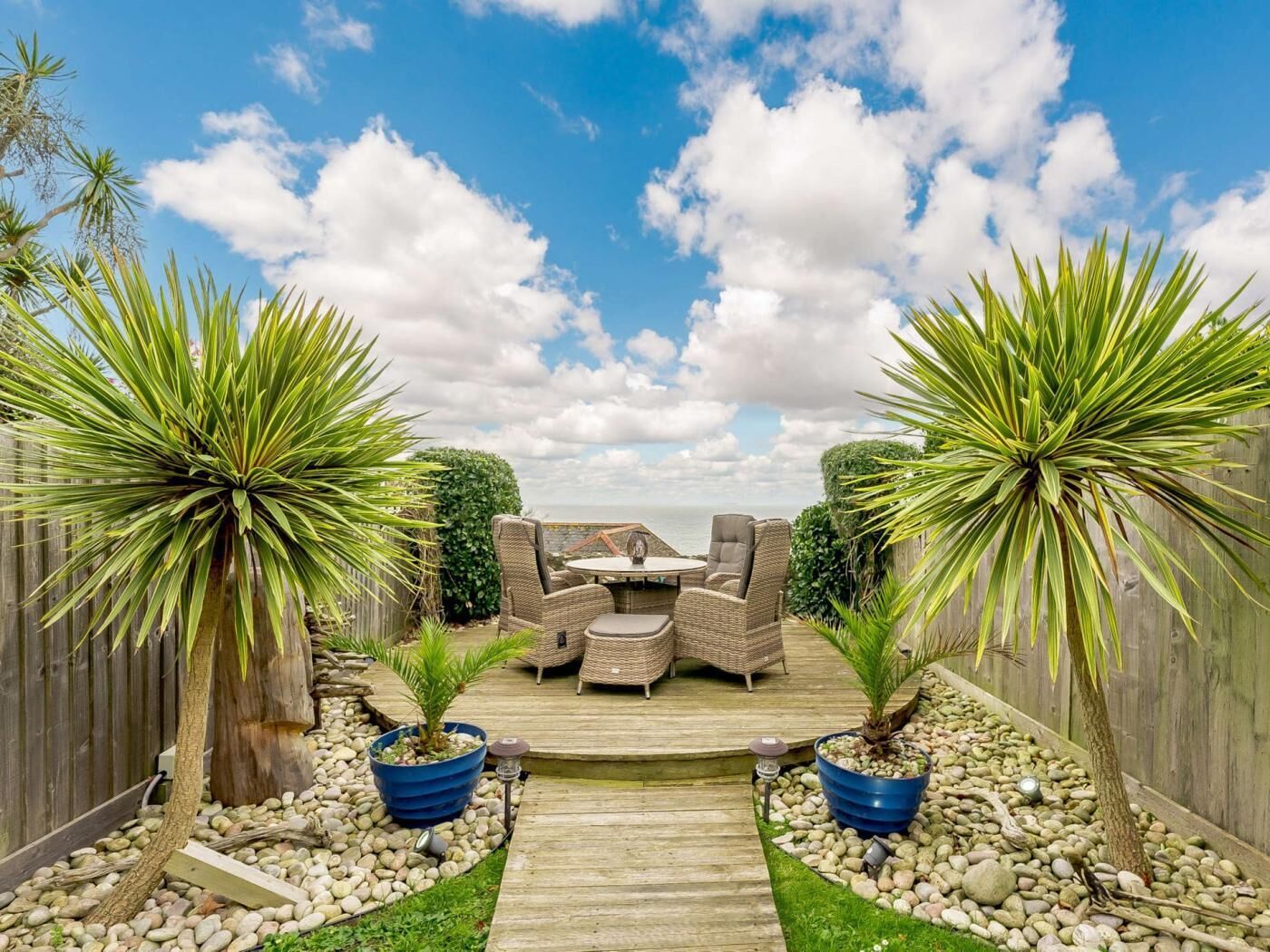 A wooden deck with outdoor furniture, surrounded by a wooden fence and tropical plants.