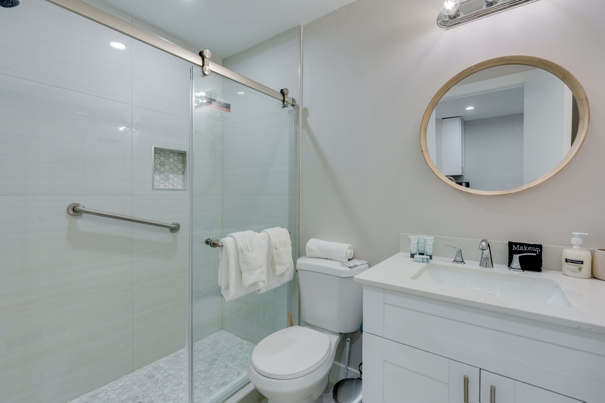 A modern bathroom with a glass shower enclosure, a white toilet, a vanity with a sink, and a round mirror.