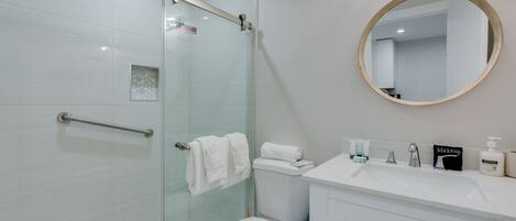A modern bathroom with a glass shower enclosure, a white toilet, a vanity with a sink, and a round mirror.