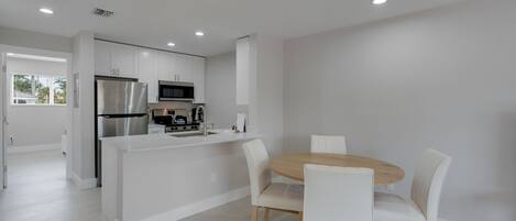 Una cocina moderna con armarios blancos, electrodomésticos de acero inoxidable y una isla central con asientos.
