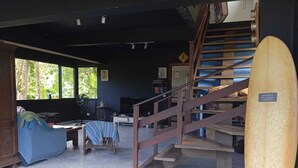 Una habitación con escalera, una tabla de surf y una ventana con vista a árboles.