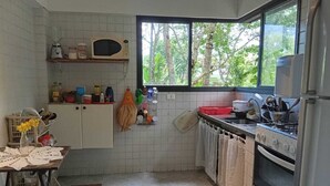 Cocina compacta con paredes de azulejos blancos, microondas, cocina a gas y ventana con vistas a zonas verdes.