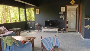 Una sala de estar con sofá, una mesita, televisor y ventilador.