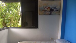 Una habitación con cama, ventana, un cuadro y vista a follaje.