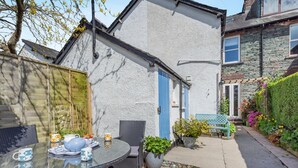 A patio with a glass table and chairs, a blue door, and a stone building in the background. - 3 Bed in Keswick (oc-89526) (Keswick)