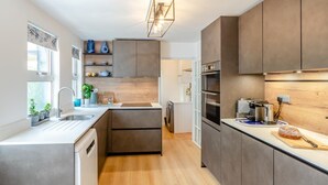 A modern kitchen with a built-in oven, a sink, and a countertop with a bread loaf. - 3 Bed in Keswick (oc-89526) (Keswick)