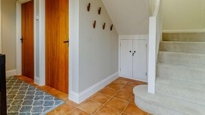 Un passadís amb portes de fusta, paret blanca amb elements decoratius, terra de rajola i una escala.