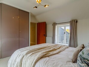 Een slaapkamer met een bed, een kledingkast, een raam met gordijnen en een plafondlamp.