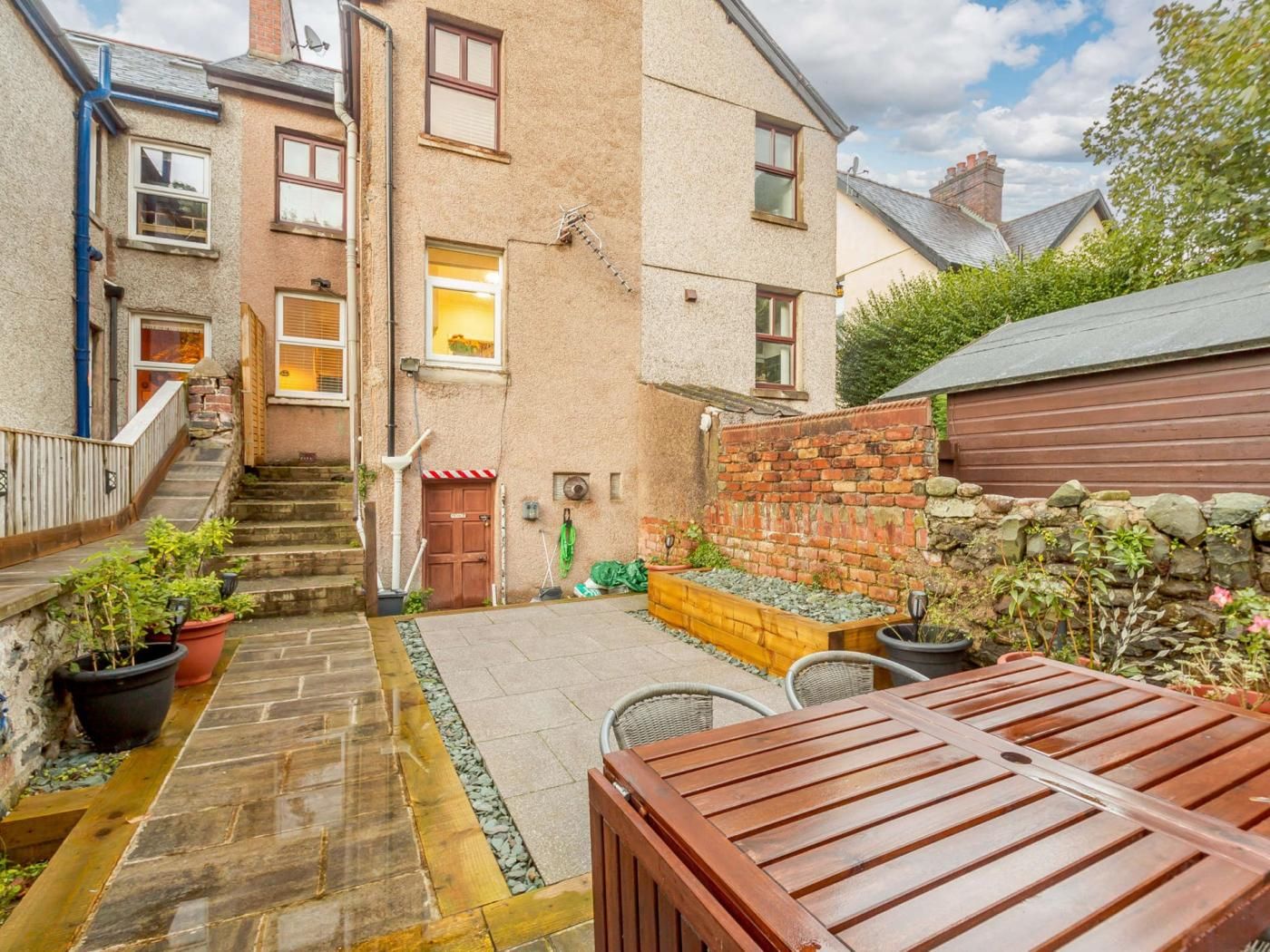 A courtyard with a wooden table, potted plants, and a brick wall.